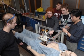 Senior Paul Blascovich watches surgical robot operating from left, while teaching assistant Lael Odhner plays with arm. Junior Tony McDonald watches from back, Junior Ian Rust and instructor Harrison Chin watch from center and right of "patient."