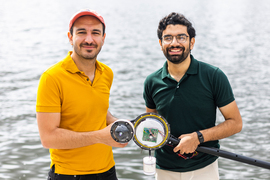 Fadel Adib and Waleed Akbar hold a small electronic device with water in background.