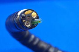 Closeup of the end of an endoscope shows sensors and three nozzles, one filled with neon-green material.