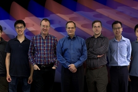 Members of the team that discovered and demonstrated the new way to trap light. From left: Bo Zhen, Chia Wei Hsu, Steven Johnson, John Joannopoulos, Marin Solja&#269;i&#263;, Song-Liang Chua and Jeongwon Lee. The background is a snapshot of a theoretical simulation of their system, where light (its electric field shown in blue and red patterns) is confined in a slab with periodic array of holes.