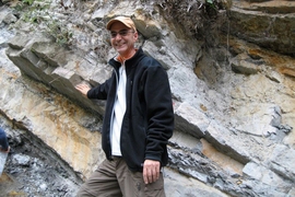 MIT professor of geophysics Daniel Rothman stands next to part of the Xiakou formation in China. His right hand rests on the layer that marks the time of the end-Permian mass extinction event. Samples from this formation provided evidence for large amounts of nickel that were spewed from volcanic activity at this time, 252 million years ago.