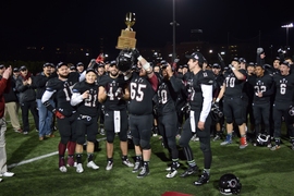 MIT players hold up the New England Football Conference trophy.