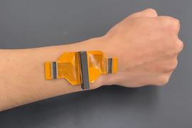 A sticker prototype is adhered to an arm, and it is about three centimeters wide and orange with gray rectangular connections.